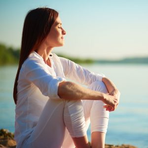 Woman sitting on beach with eyes closed