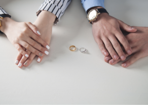 Man and woman's hands sitting on table with wedding rings laying between them.