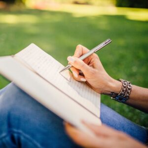 Woman sitting on grass writing in journal
